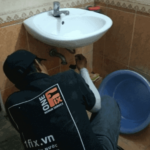 Thợ đang kiểm tra và thông nghẹt hệ thống xi-phông bên dưới bồn rửa mặt lavabo.