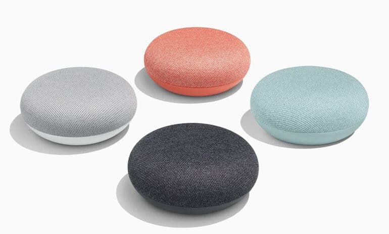 Google Home Mini màu xám được đặt trên bàn gỗ, bên cạnh một chậu cây nhỏ, tạo cảm giác thân thiện và hiện đại.