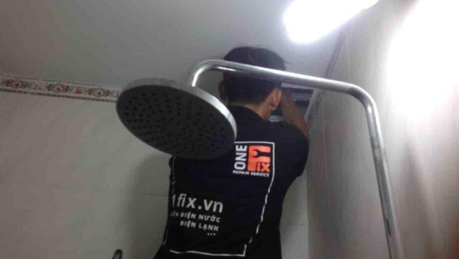 Thợ đang siết chặt khớp nối vòi sen vào đường ống nước trên tường.