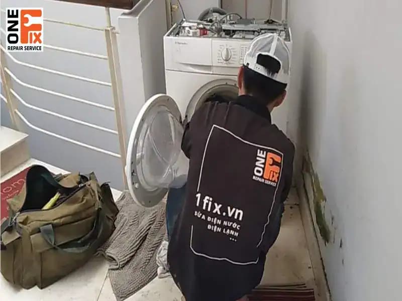 Thợ 1Fix đang kiểm tra phần động cơ và dây curoa phía sau máy giặt.