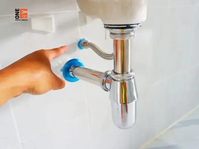 Một thợ sửa ống nước chuyên nghiệp đang làm việc dưới gầm chậu rửa bát, thể hiện quá trình lắp đặt và căn chỉnh đường ống.