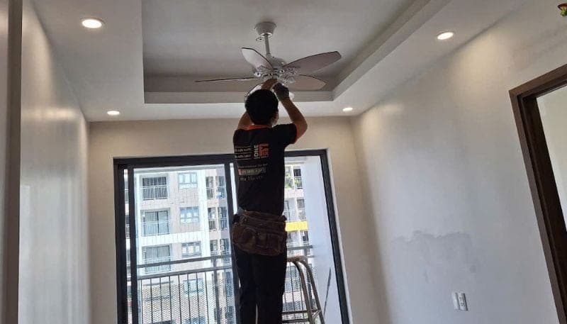 Thợ đang dùng tay cân chỉnh lại một chiếc quạt trần Panasonic bị lắc.